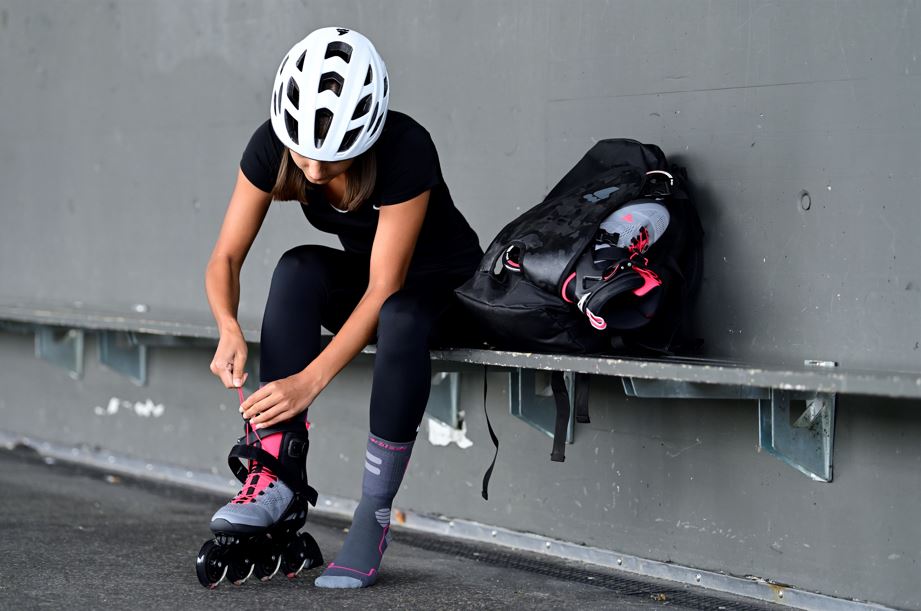 women sitting and putting on her rollerblades with her bag carrying inline skates